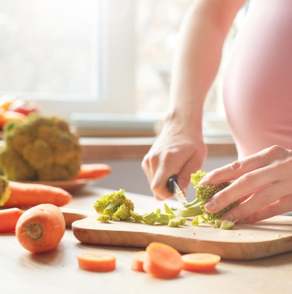 Young pregnant woman in the kitchen at home maternity concept cooking salad close-up near window